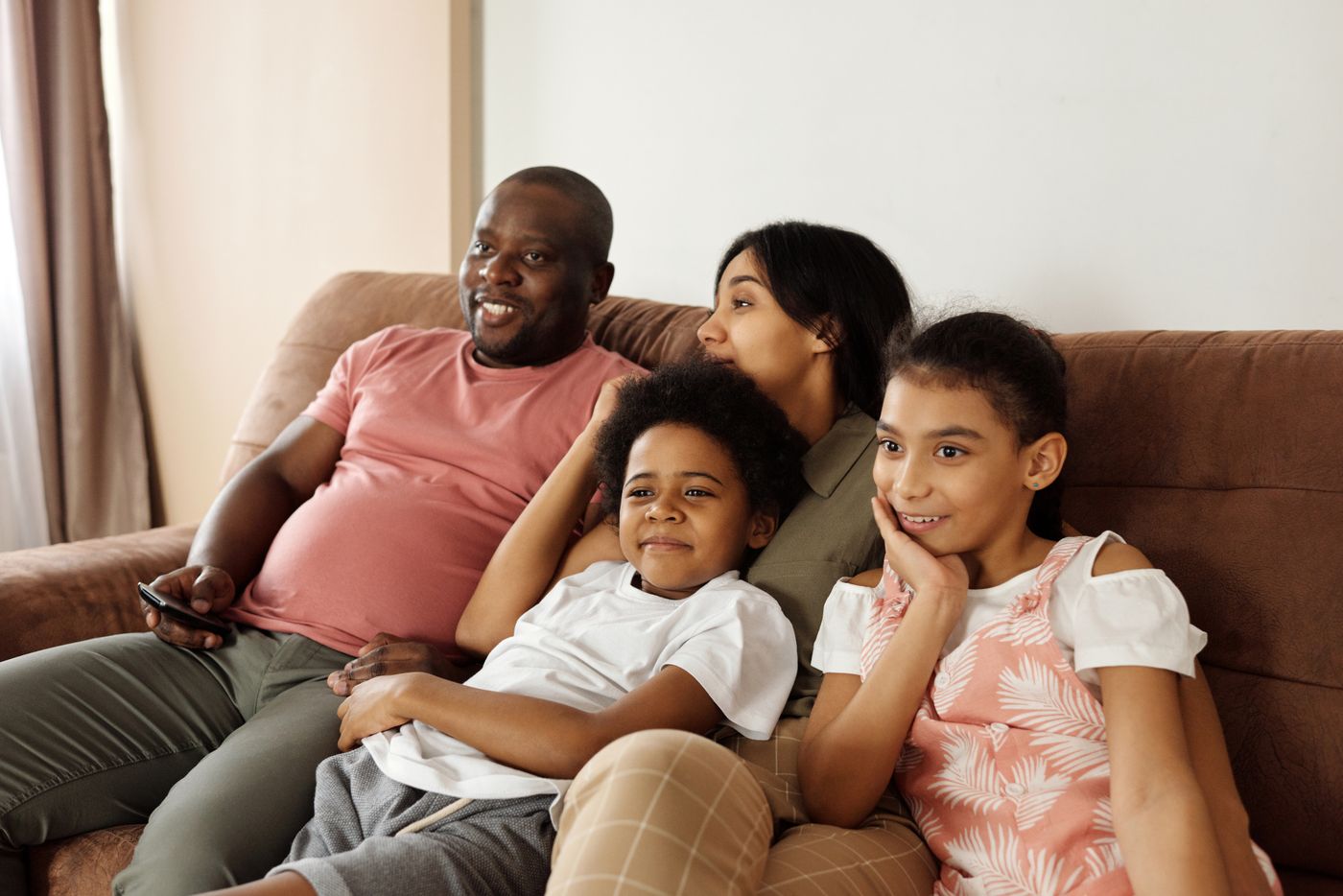 A family of four sitting together on a living room couch watching a game on television