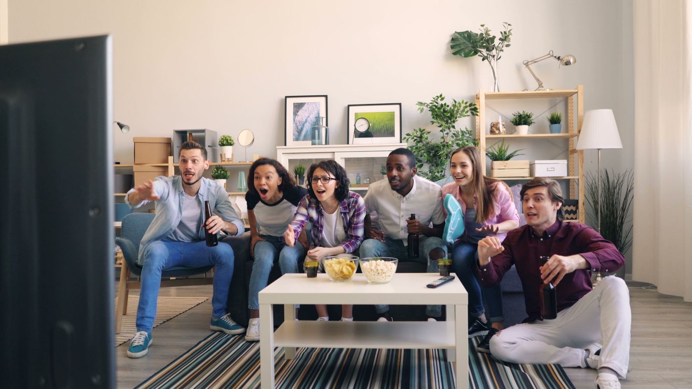 A group of friends gathered around a living room television reacting to a sports game